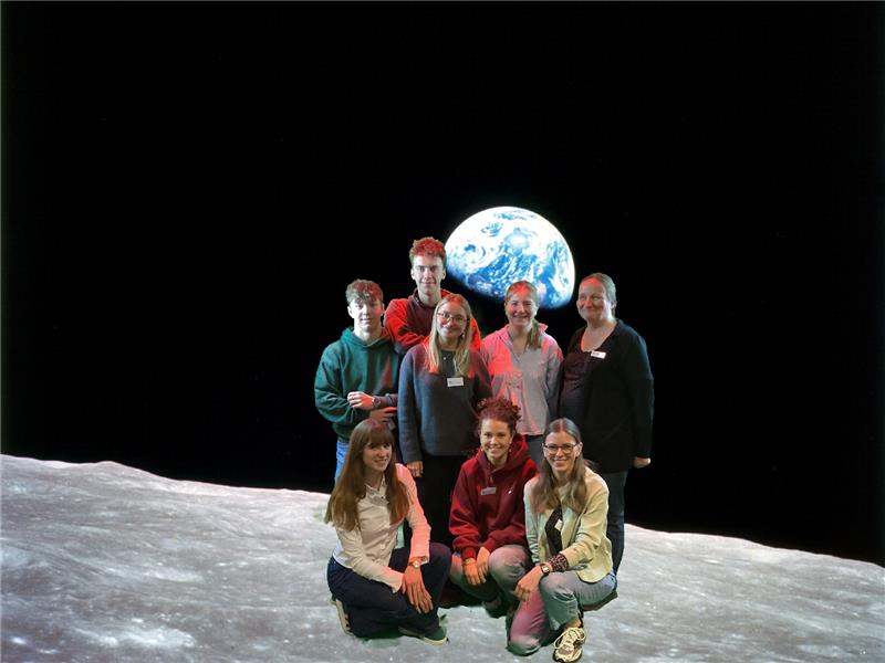 Zu sehen ist eine digital bearbeitete Mondlandschaft mit einer achtköpfigen Gruppe bestehend aus Schülerinnen und Schülern der Oberstufe mit ihren Lehrerinnen. 